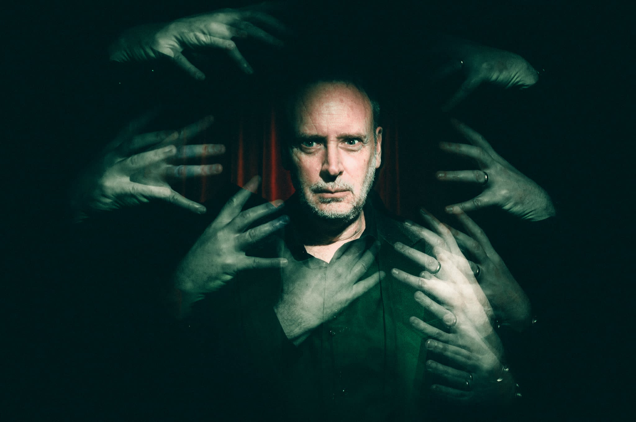Kevin Kopfstein surrounded by ghostly disembodied hands reaching from the darkness.