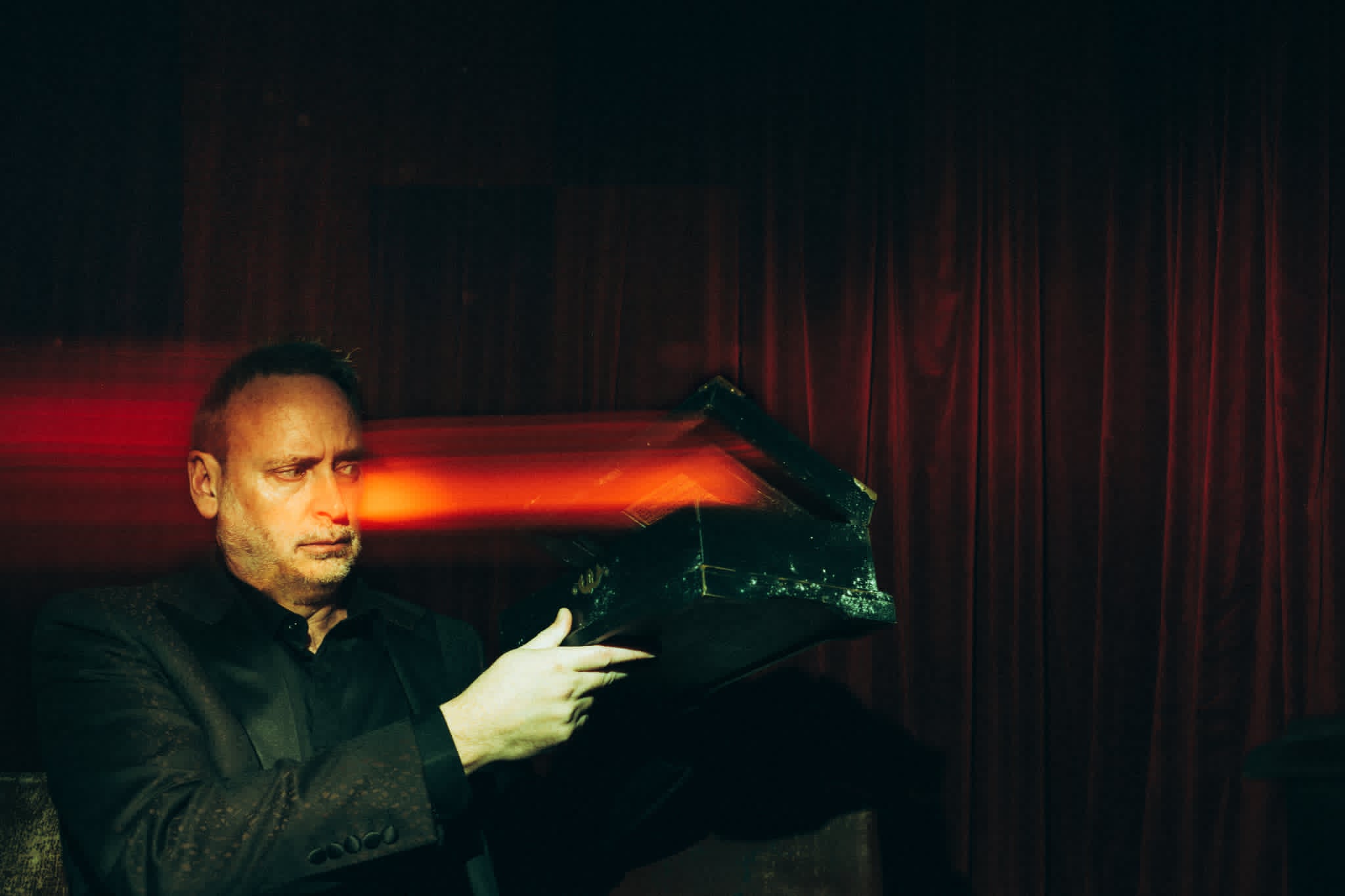 Kevin Kopfstein cradling a glowing accursed relic box as red light streaks through the dark.