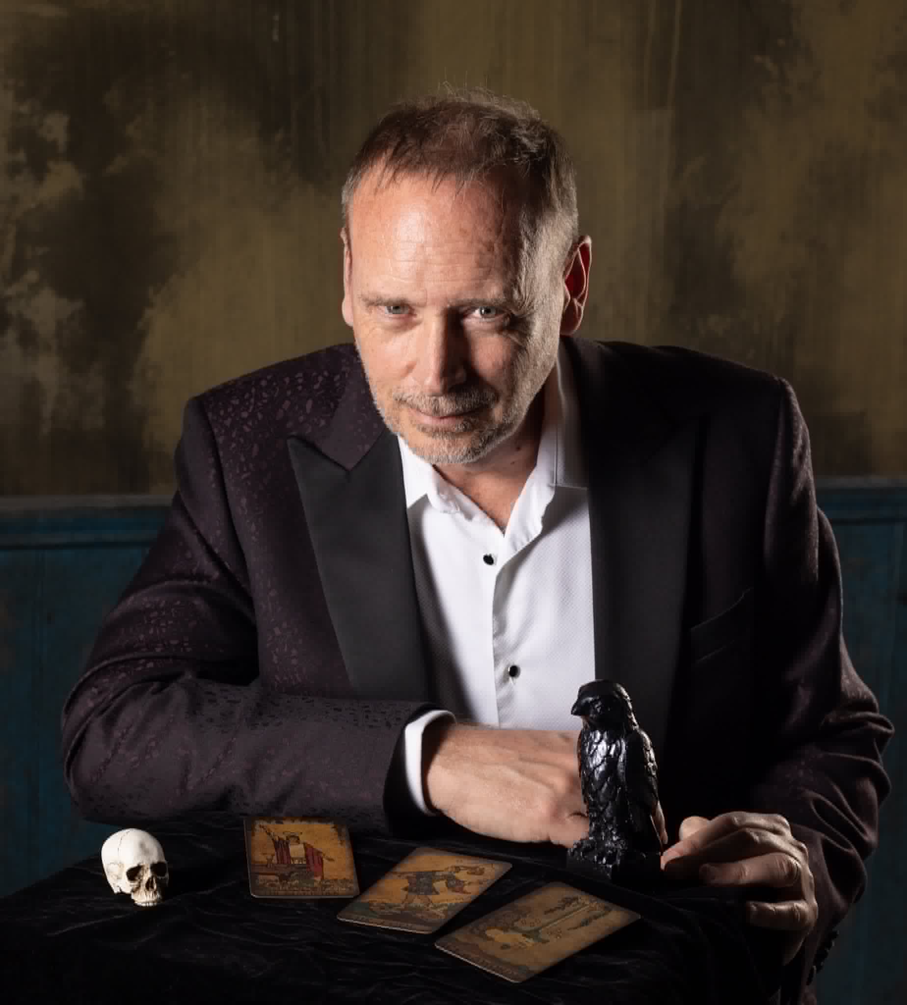 Kevin Kopfstein at a séance table with a raven figurine, a small skull and spread tarot cards.